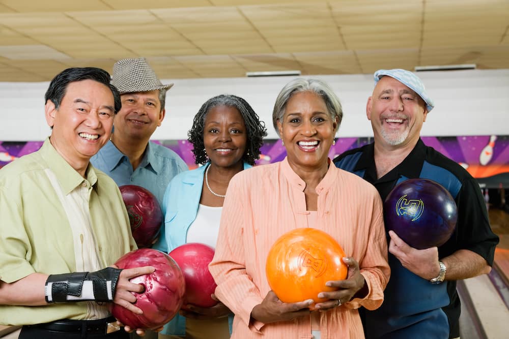 A group of elderly friends holding bowling balls in bowling alley