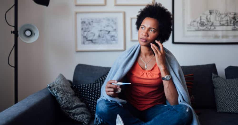 Black woman on call holding cup, seated on the couch looking outside. Photo for illustration.
