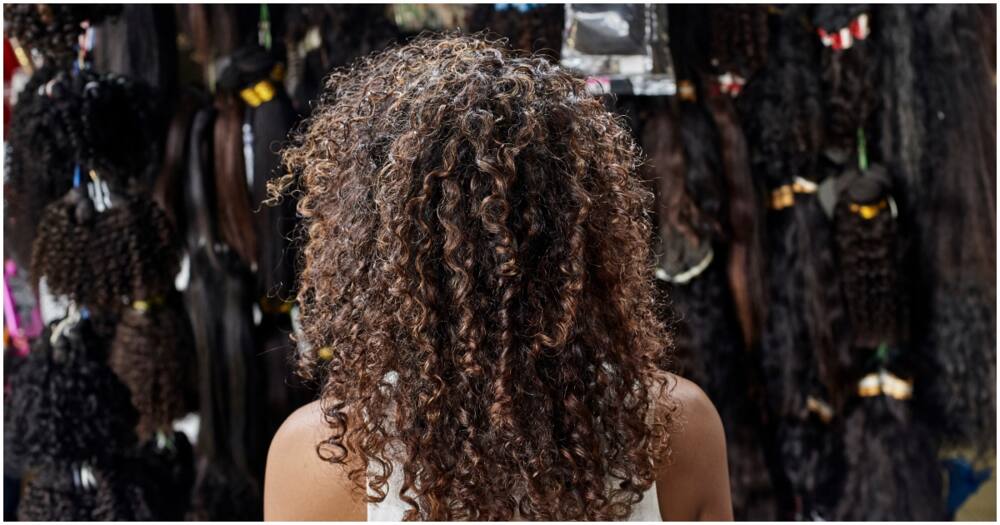 Young African woman from behind with curly hair in a wig shop. Photo: Getty Images.