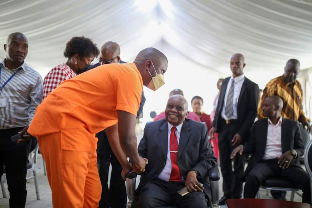 Former president Armando Guebuza, seated, greets his son Ndambi, a defendant in the corruption trial