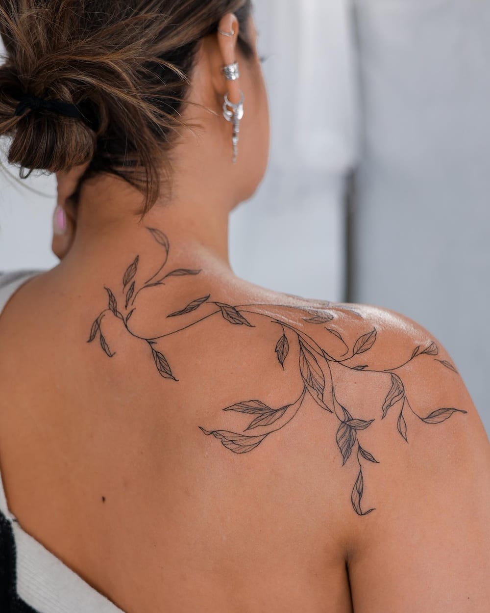 A woman with a vine shoulder wrap tattoo on her back.
