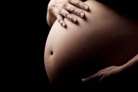 A pregnant African woman with her hands on her back smiling into the distance. Photo: Getty Images.