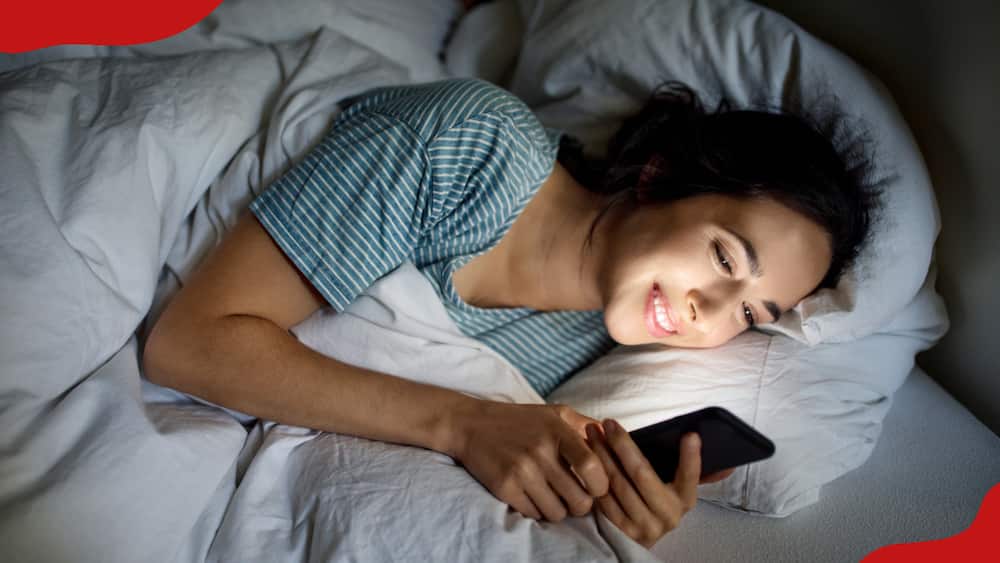 A woman smiling while using her phone on the bed