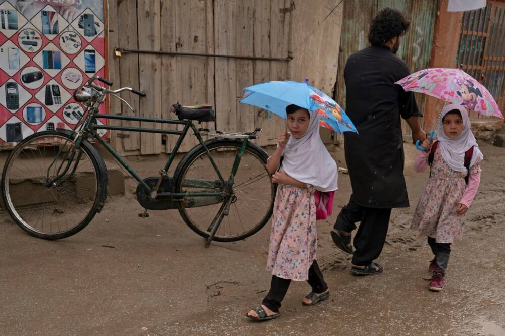 Afghan girls hold umbrellas as they walk along a street in Parwan province on August 25, 2022