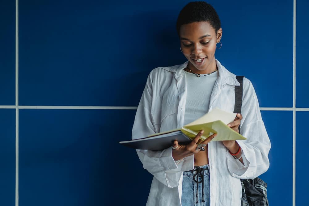A young woman in a white shirt and denim pants is reading a book