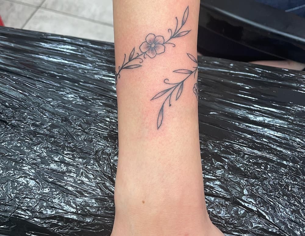 Minimalistic flower wrist tattoo on a person's arm with delicate vine patterns.