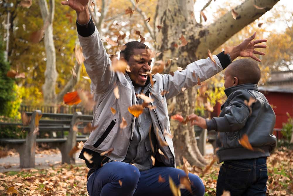 Young man and toddler son throwing autumn leaves in park.