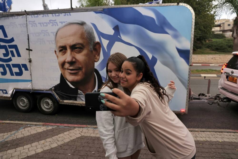 Two girls pose for a selfie photo before a vehicle showing Israel's former prime minister Benjamin Netanyahu, ahead of November 1 general elections
