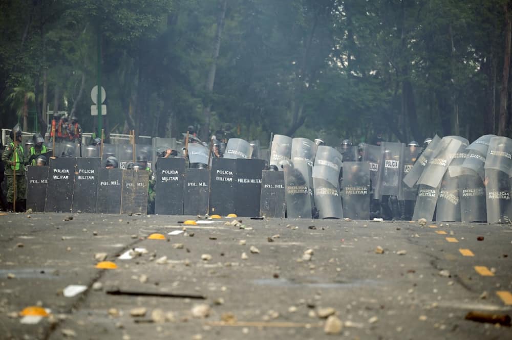 Mexican military police take cover from stones and homemade explosive devices thrown during a demonstration at an army camp over the disappearance of 43 students in 2014