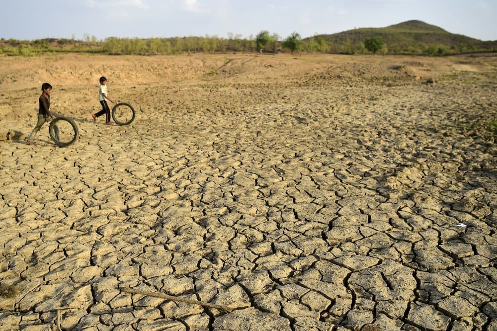 Children play with discarded cycle tyres as they walk on a dried up pond in Agrotha