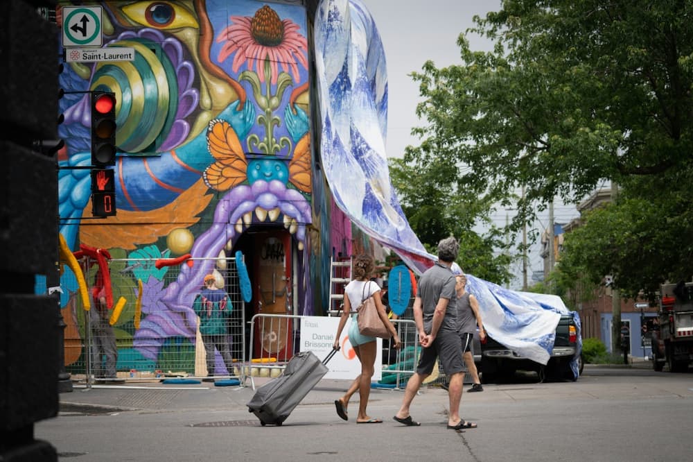 People watch artists at work during the tenth edition of the Mural festival in Montreal, Quebec on June 16, 2022