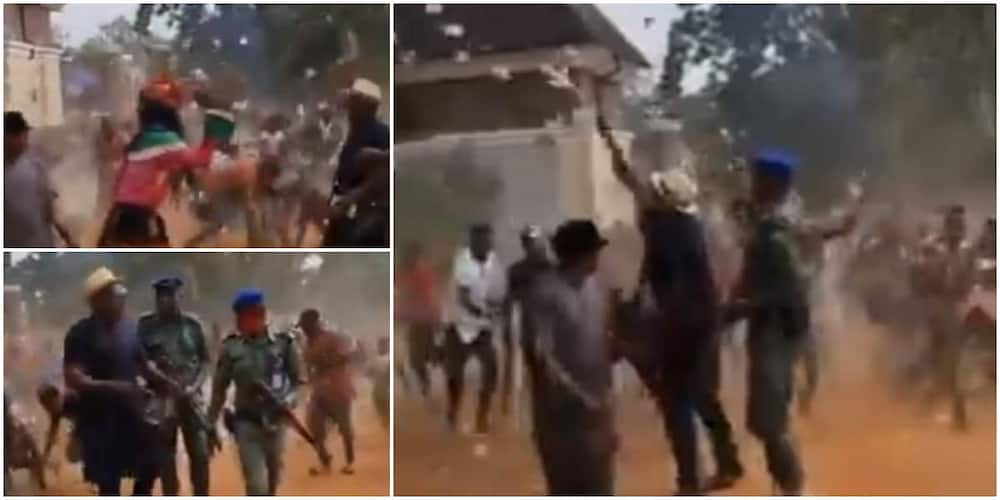 Reactions as masquerade, others jostle to pick cash as man sprays money on street.