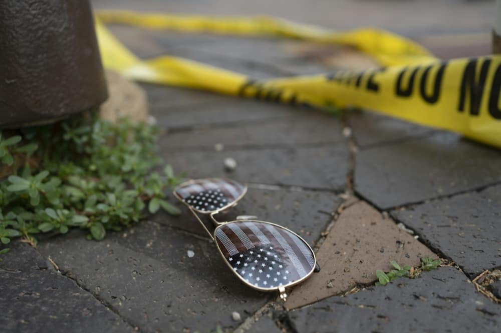 Police crime tape is seen near an American flag-themed sunglasses laying on the ground at the scene of the Fourth of July parade shooting in Highland Park, Illinois on July 4, 2022