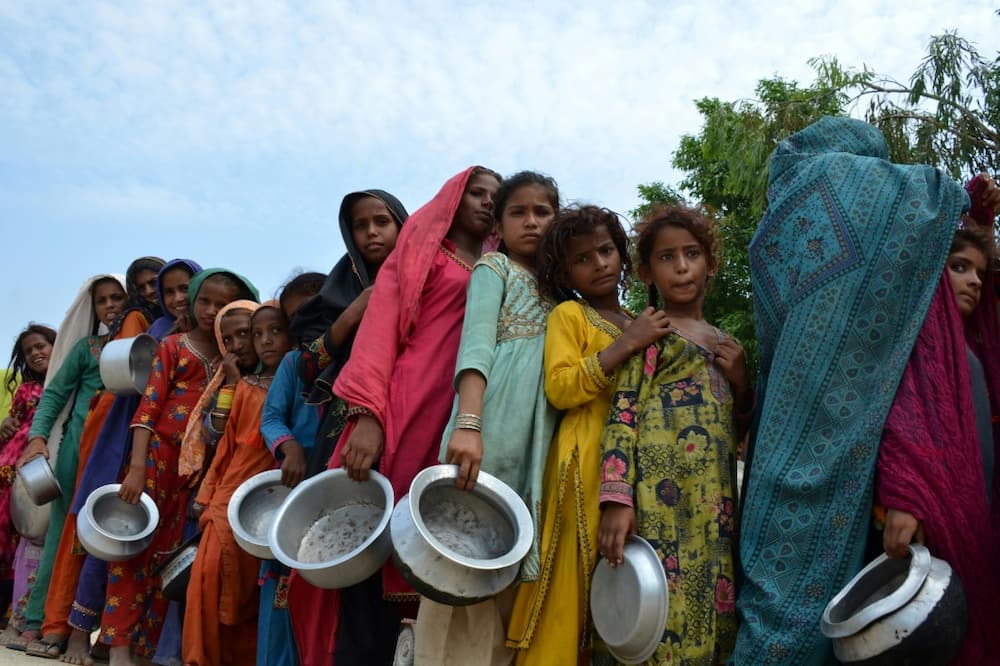 Displaced flood-affected people stand in a queue to receive food at a makeshift camp in flood-hit Sehwan, Pakistan