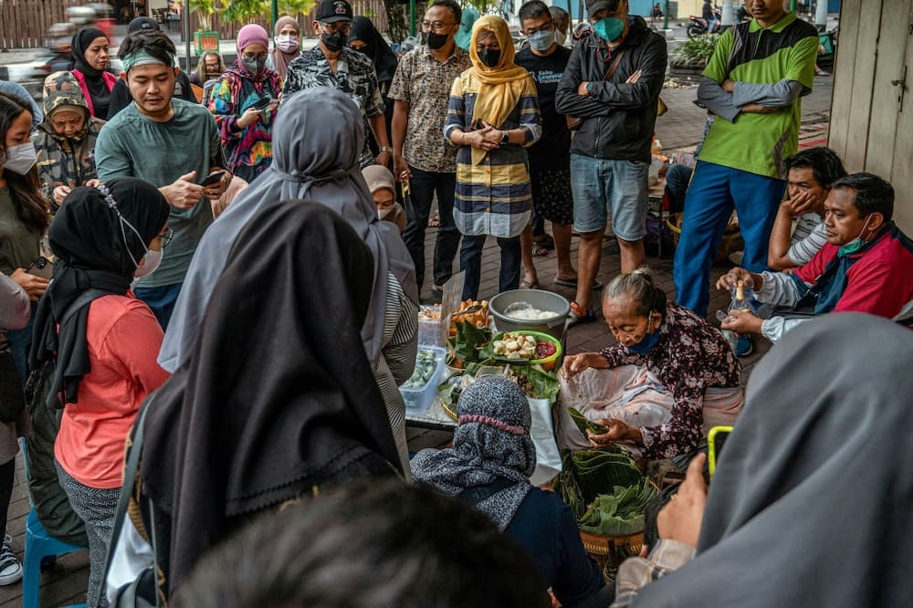 As the morning twilight approaches in an Indonesian city famed for its street food scene, customers gather around Mbah Satinem as she prepares her famous lupis