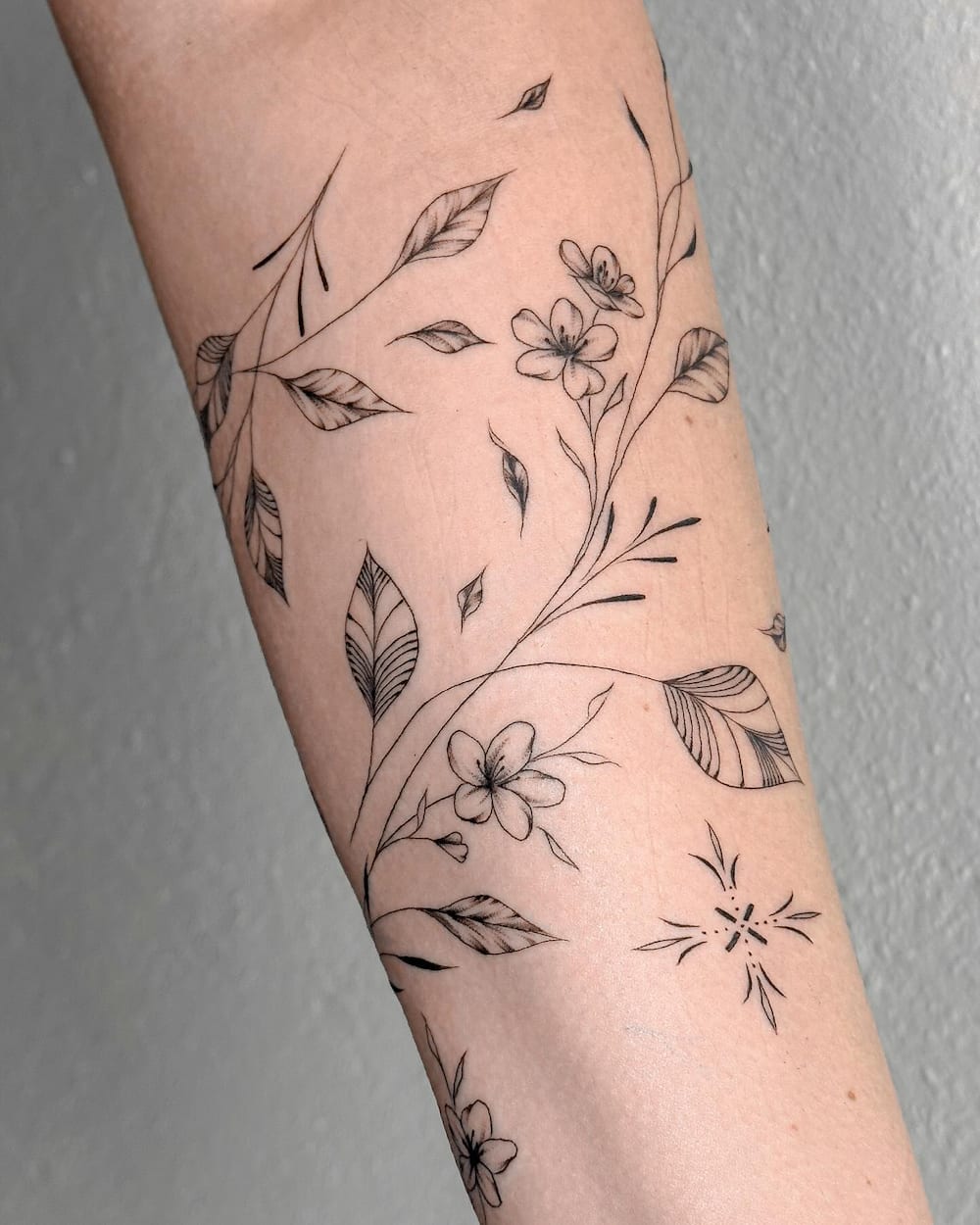Monochrome vine tattoo with floral and leaf motifs on the arm.