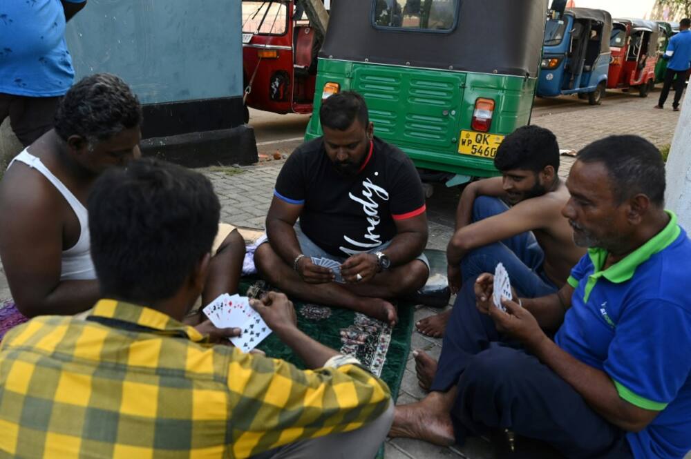 Out of gas and stuck in line for days, a group of motorists kick off their shoes and settle on a sidewalk in Sri Lanka's capital for a round of cards while waiting for fuel