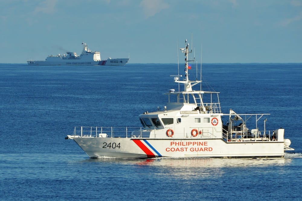 A Philippines coast guard ship (R) sails past a Chinese coast guard ship near Scarborough Shoal in the South China Sea in 2019