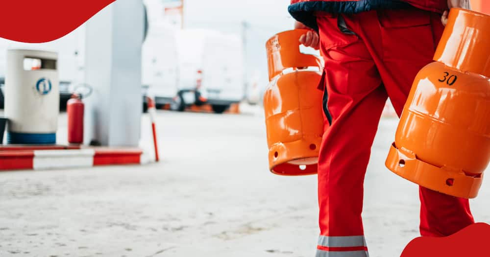 Close up waist down photo of a gas station worker holding two big orange gas cylinders.