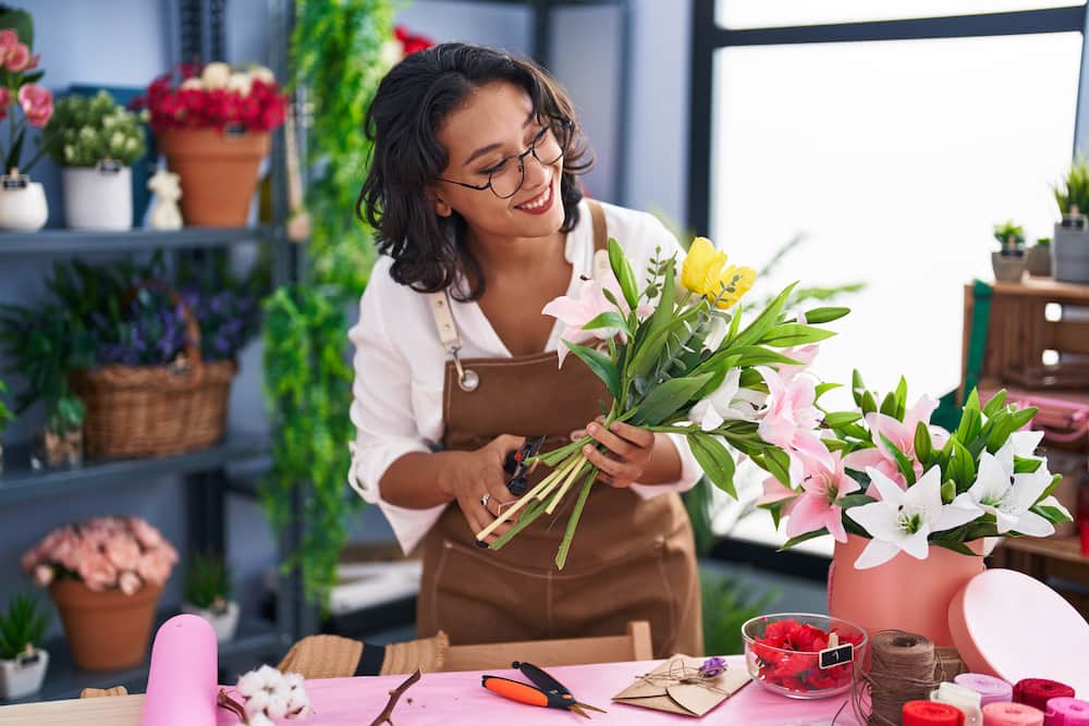 Young beautiful Hispanic woman florist makes bouquets of flowers at a flower shop