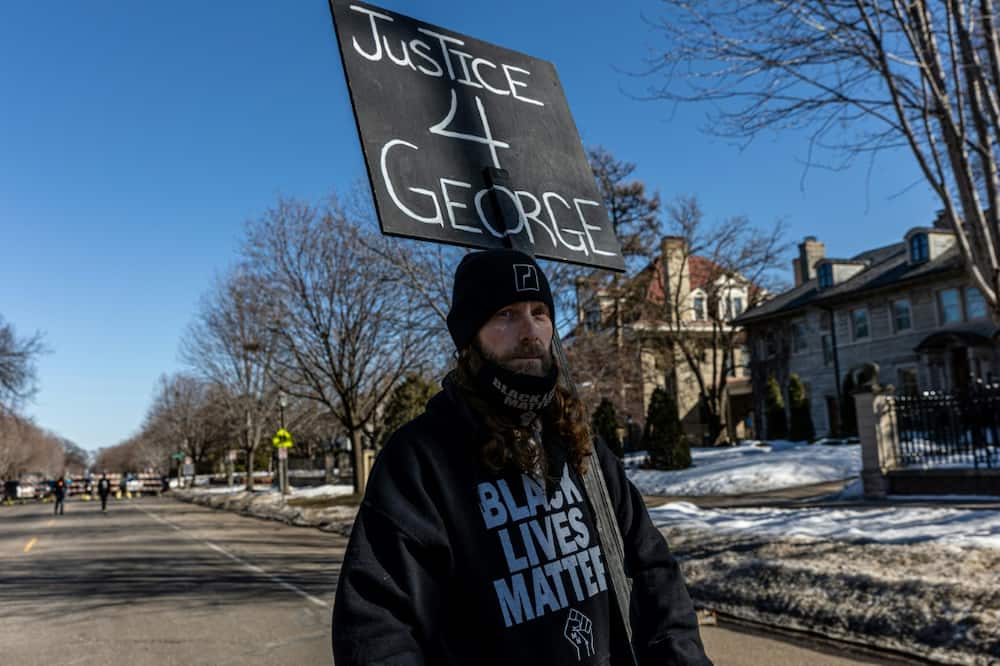 A man holds a placard outside the Minnesota governor's residence during a protest on March 6, 2021; a UN group of experts was appointed after Floyd's murder to investigate global systemic racism