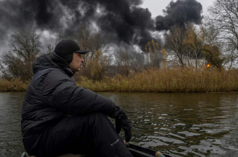 A fisherman sails his boat on the Dnipro River as black smoke rises from an oil depot in Kherson, on November 20, 2022, amid the Russian invasion of Ukraine