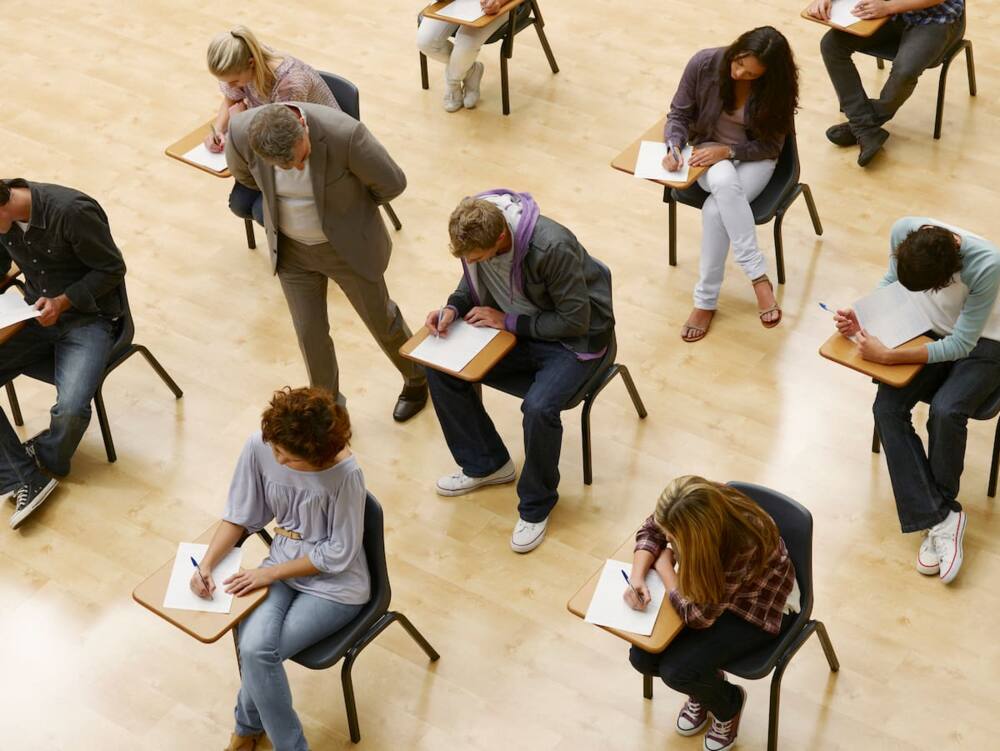 Professor walking by college students taking test in classroom