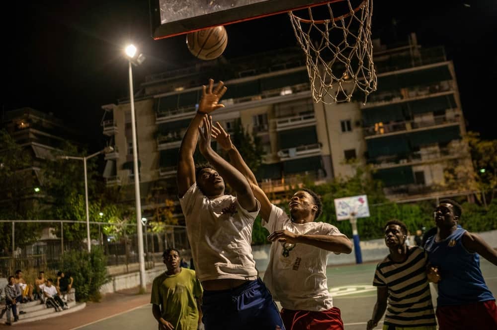 Young Athenians sharpen their shooting skills under the dazzling white lights of an outdoor basketball court