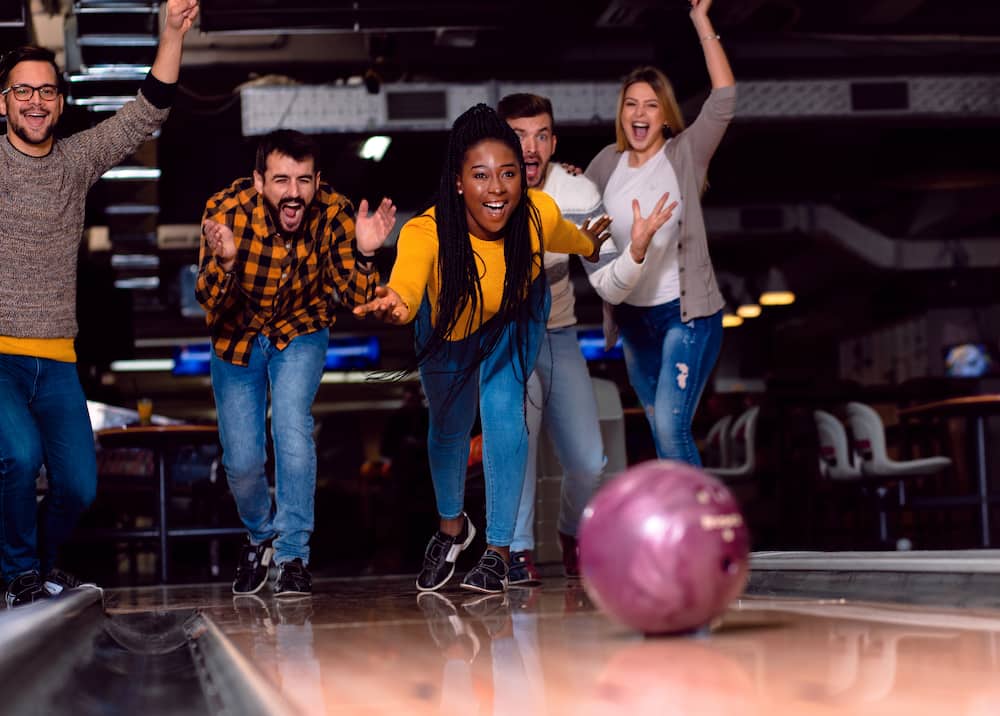 A woman is cheered by her friends as she bowls at a bowling alley.