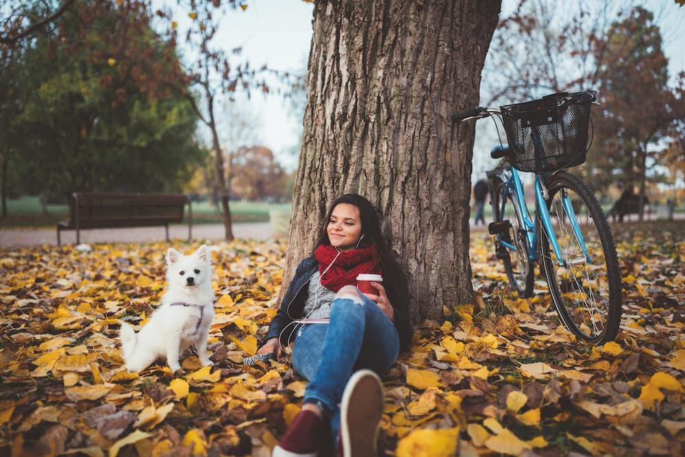 Relaxed girl with her dog drinking coffee in the park.