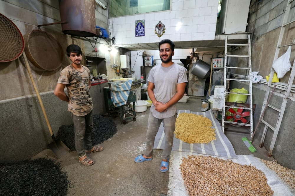 Roaster Majid Ebrahimi (R) and a worker pose for a picture in front of their roasting machine in Tehran's Grand Bazaar