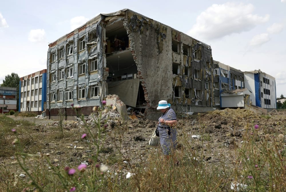 A woman walks past a school partially destroyed by a missile