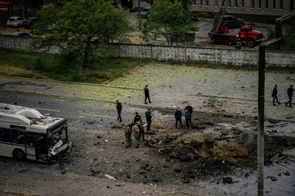 Investigators examine a crater next to a damaged bus following a missile strike in the town of Dnipro