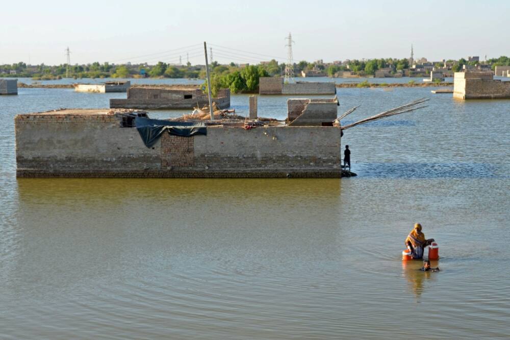 A woman wades through the flood waters to get drinking water in Dera Allah Yar, Pakistan; fossil fuel usage is a major contributor to climate change