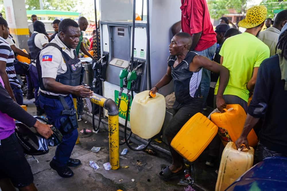 A Haitian police officer confronts people queueing to collect petrol at a gas station in Port-au-Prince on July 15, 2022