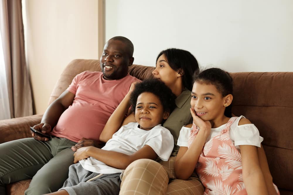 A biracial family is watching TV on a brown sofa