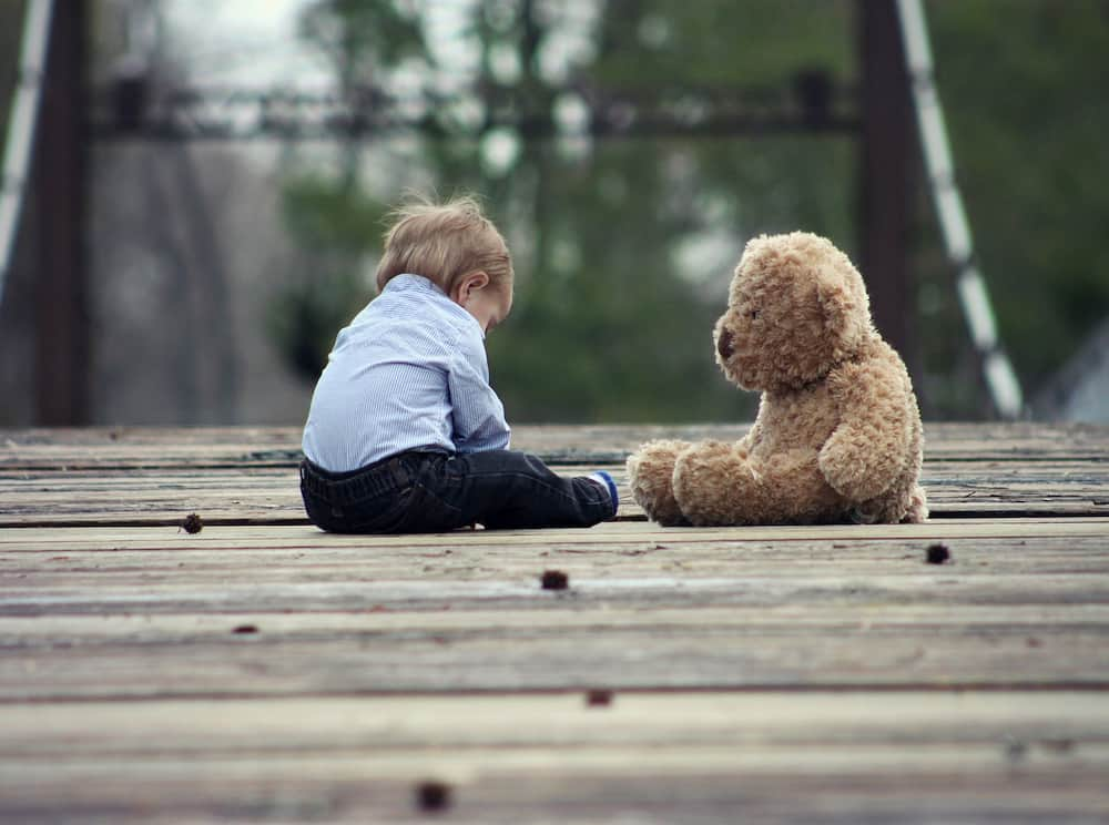 A boy is sitting with a brown teddy bear