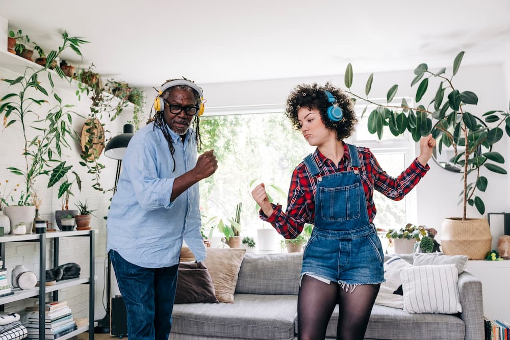 Young woman listening to music through headphones while dancing with father at home.