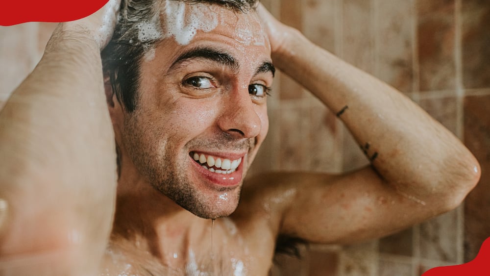 A man stands in the shower, scrubbing his head and creating a lather with the shampoo.