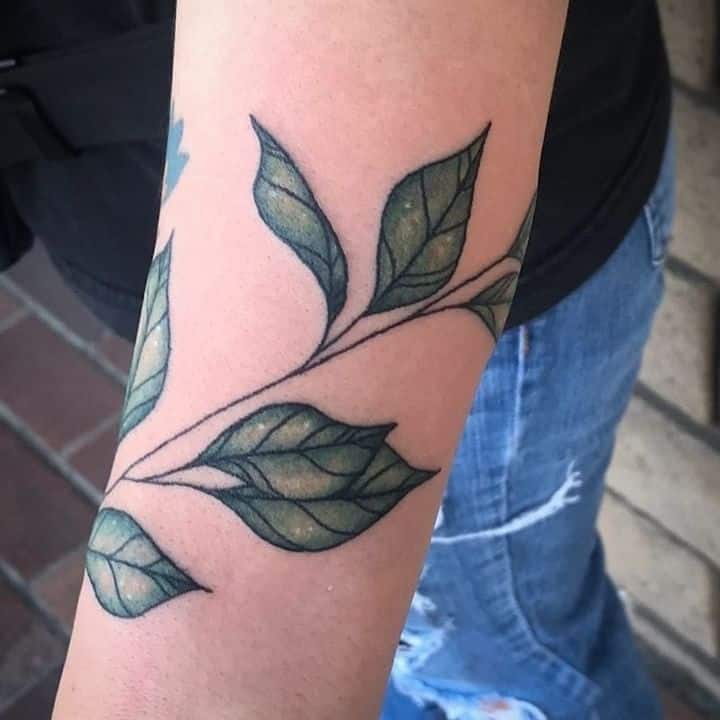 Arm tattoo featuring intricate leaf design, resembling wrap around greenery.