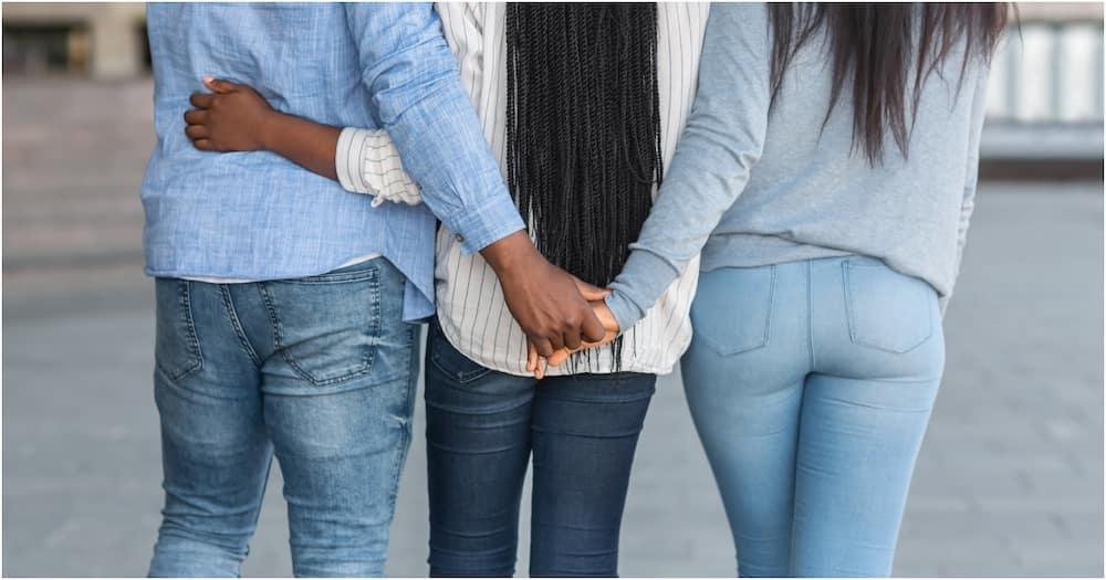 Afro guy hugging with one girl and holding hands with another. Photo: Getty Images.