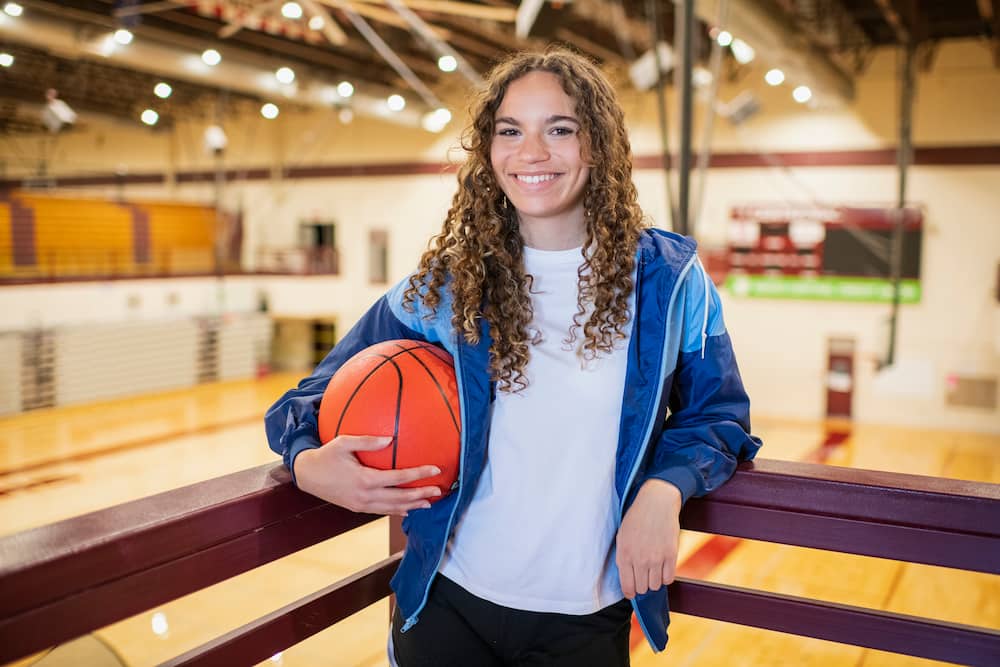 Portrait of female high school basketball player in gymnasium.