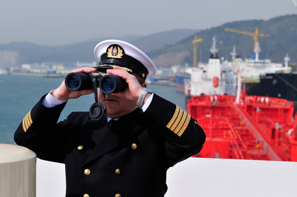 A navigation officer with binoculars is looking ahead on the navigation bridge