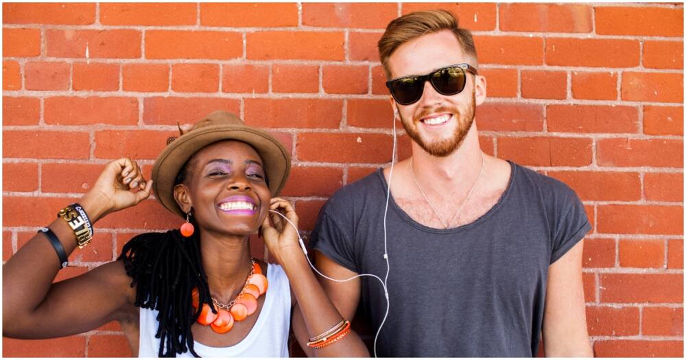 Couple listening to earbuds near brick wall. Photo: Getty Images.