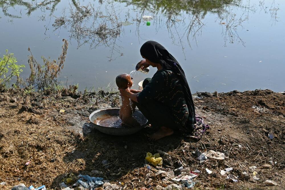 A woman bathes her child next to a flooded field in southern Pakistan