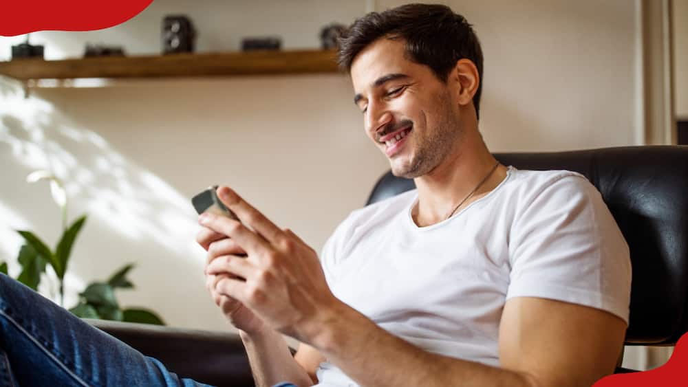 A young man relaxing on an armchair at home using a mobile phone