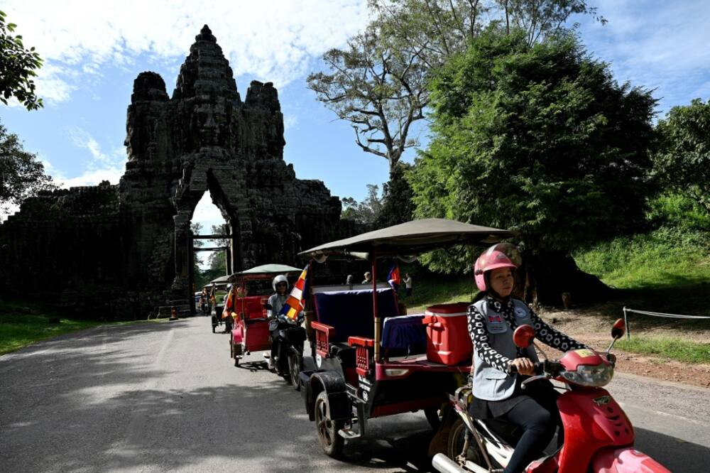 Female tuk-tuk drivers ride past the Angkor Thom south gate at the Angkor complex in Siem Reap province