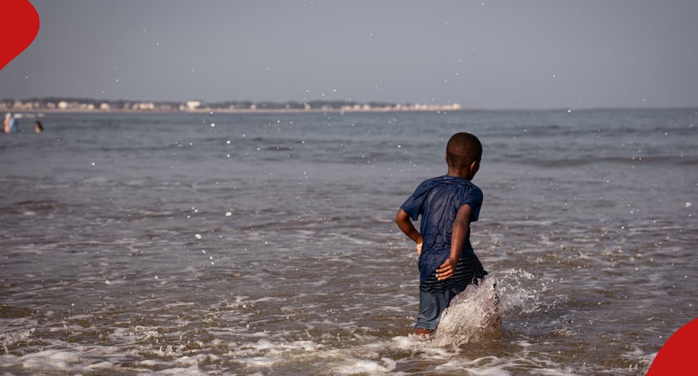 Black child plays on the beach and in the water off the coast of Maine on a summer afternoon. The boy is joyous and enjoys the warm water.