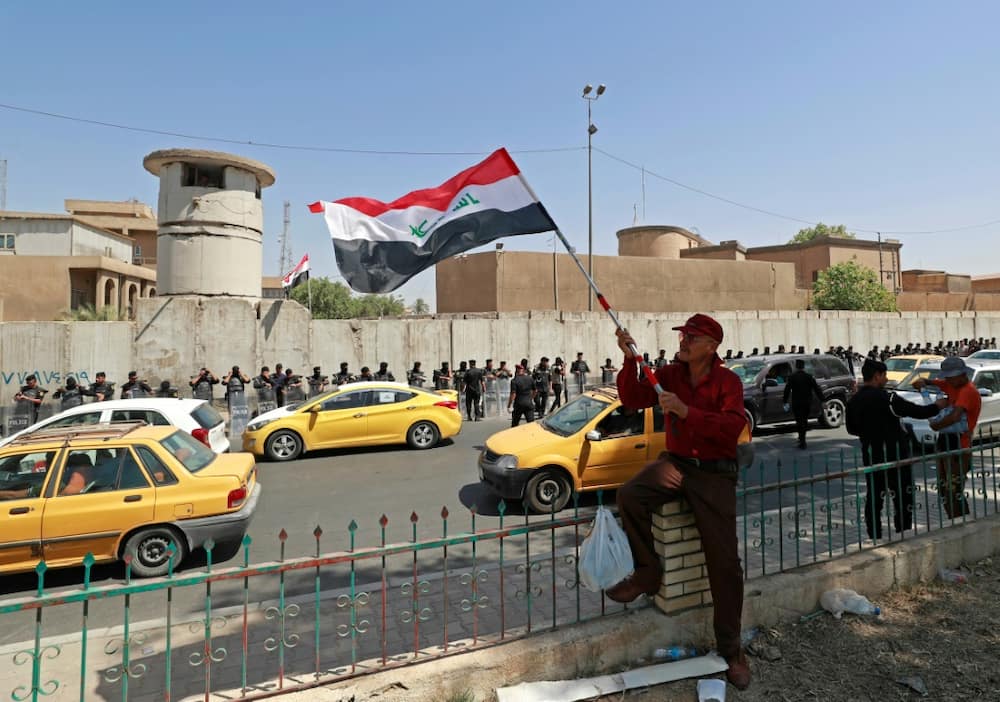 A protester waves an Iraqi national flag as security forces stand guard outside the Turkish visa office in Baghdad during a demonstration against the deadly attack in Kurdistan