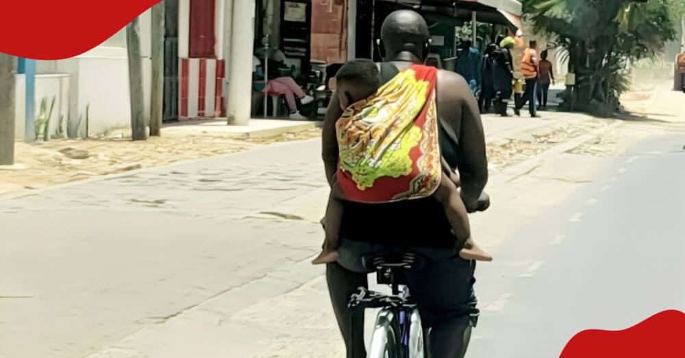 A man riding a bicycle with a baby wrapped on his back in Mombasa.